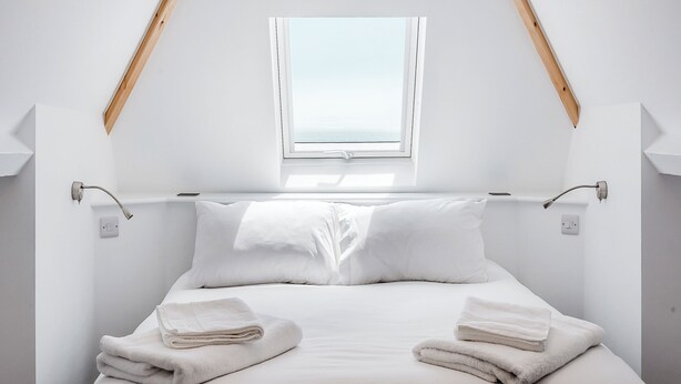 A minimalist bedroom with a sloped ceiling, a skylight, a bed with white linens, and a small window. - A stunning two-level seaside retreat with incredible sea views. (East Preston, West Sussex Coast)