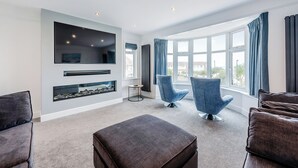 A modern living room with a large window, a fireplace, and two blue armchairs. - A stunning two-level seaside retreat with incredible sea views. (East Preston, West Sussex Coast)