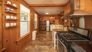 Una cucina in una casetta di legno con un fornello, un frigorifero ed scaffali con tazze.