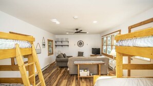 Una camera in stile dormitorio con letti a castello, un divano, una televisione e una ventola a soffitto.