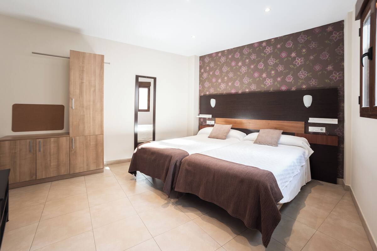 A bedroom with a large bed, a wooden wardrobe, and a mirror.