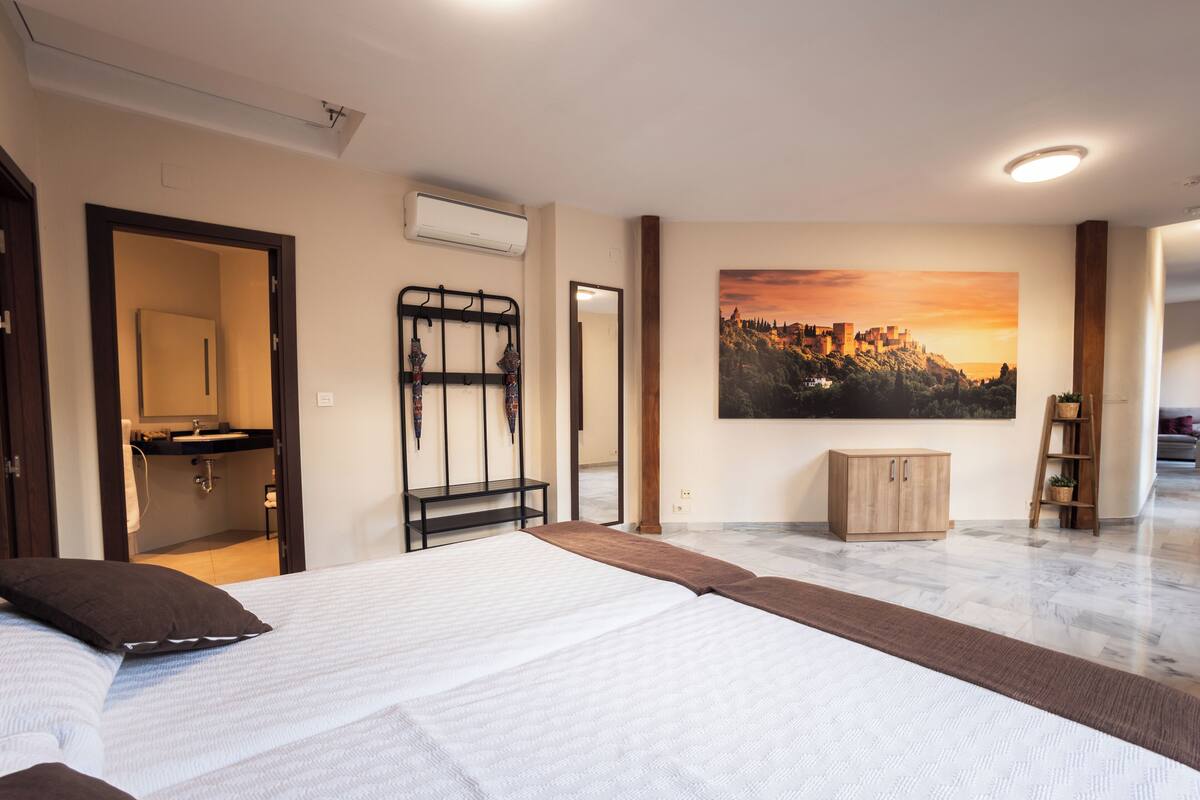 A bedroom with a bed, a bathroom, a painting of a sunset, and a wooden cabinet.