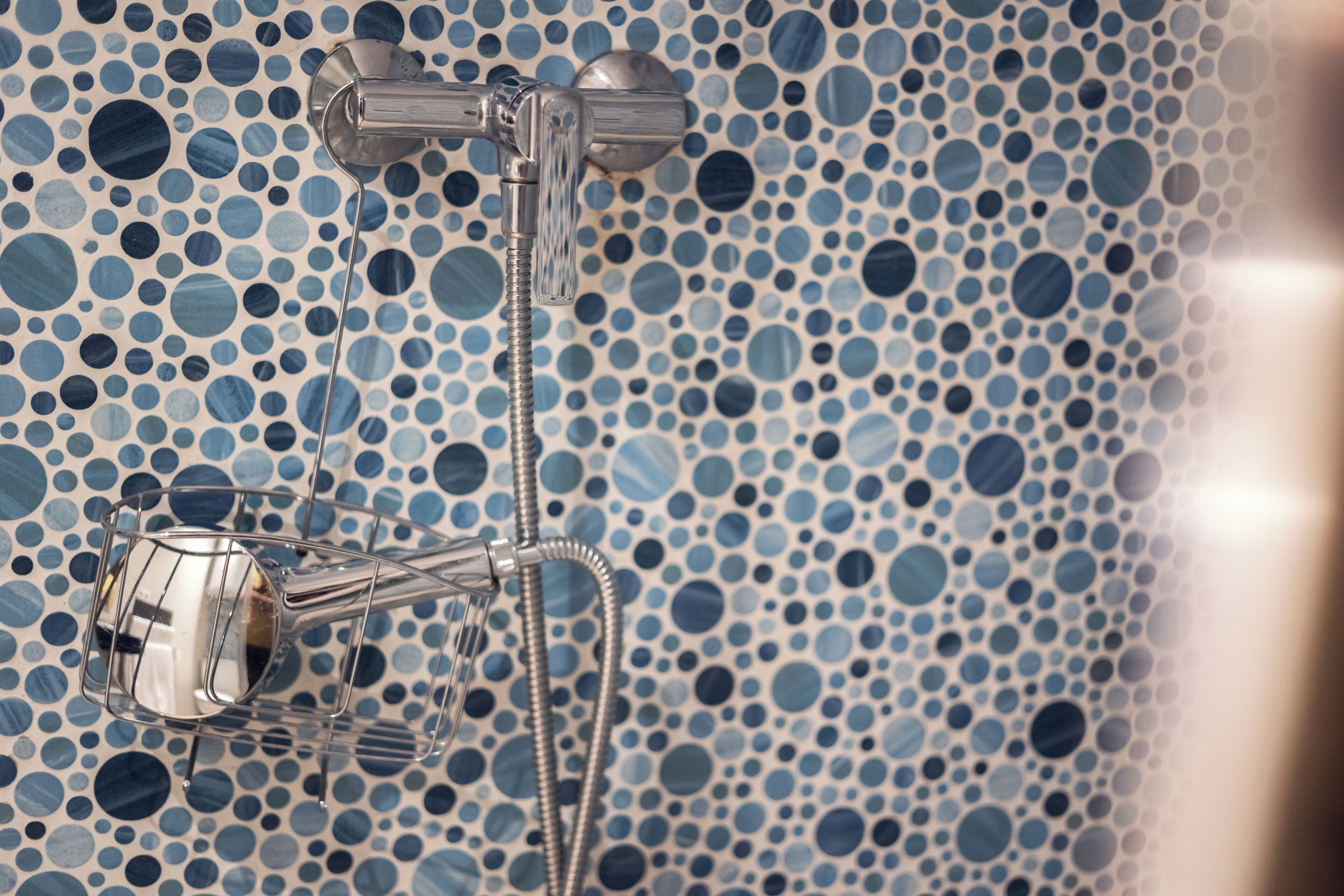 A shower with a modern design, featuring a metallic faucet and hose, set against a wall with a blue and white polka dot pattern.