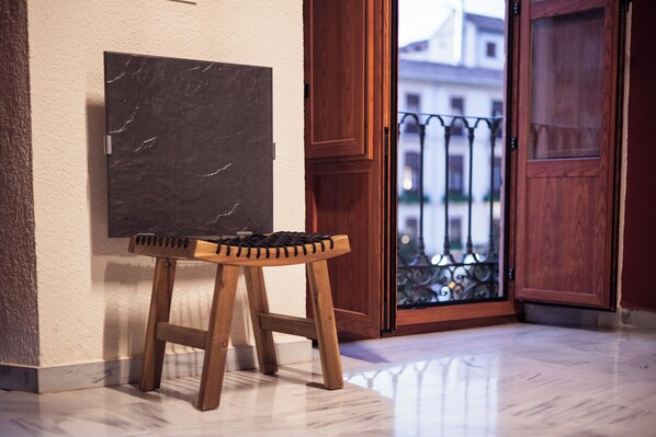 A wooden stool with a woven seat, a marble wall, a wooden door, and a balcony with a wrought iron railing.