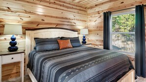A wooden-paneled bedroom with a bed, two bedside tables, and a window with curtains.