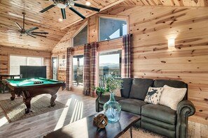 A wooden interior with a pool table, a sofa, and a vase with flowers.