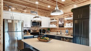 A modern kitchen with wooden paneling, stainless steel appliances, a central island with a bowl of fruit, and a coffee sign.