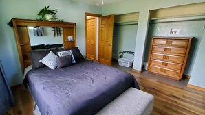 A bedroom with a bed, a wooden dresser, a wardrobe, and a plant.