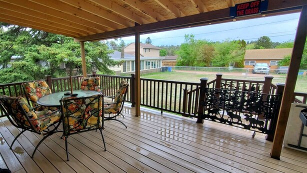 A covered outdoor patio with a wooden table and chairs, a metal railing, and a view of a residential street.