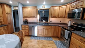 A kitchen with wooden cabinets, a dishwasher, a microwave, an oven, and a dining area with a table and chairs.