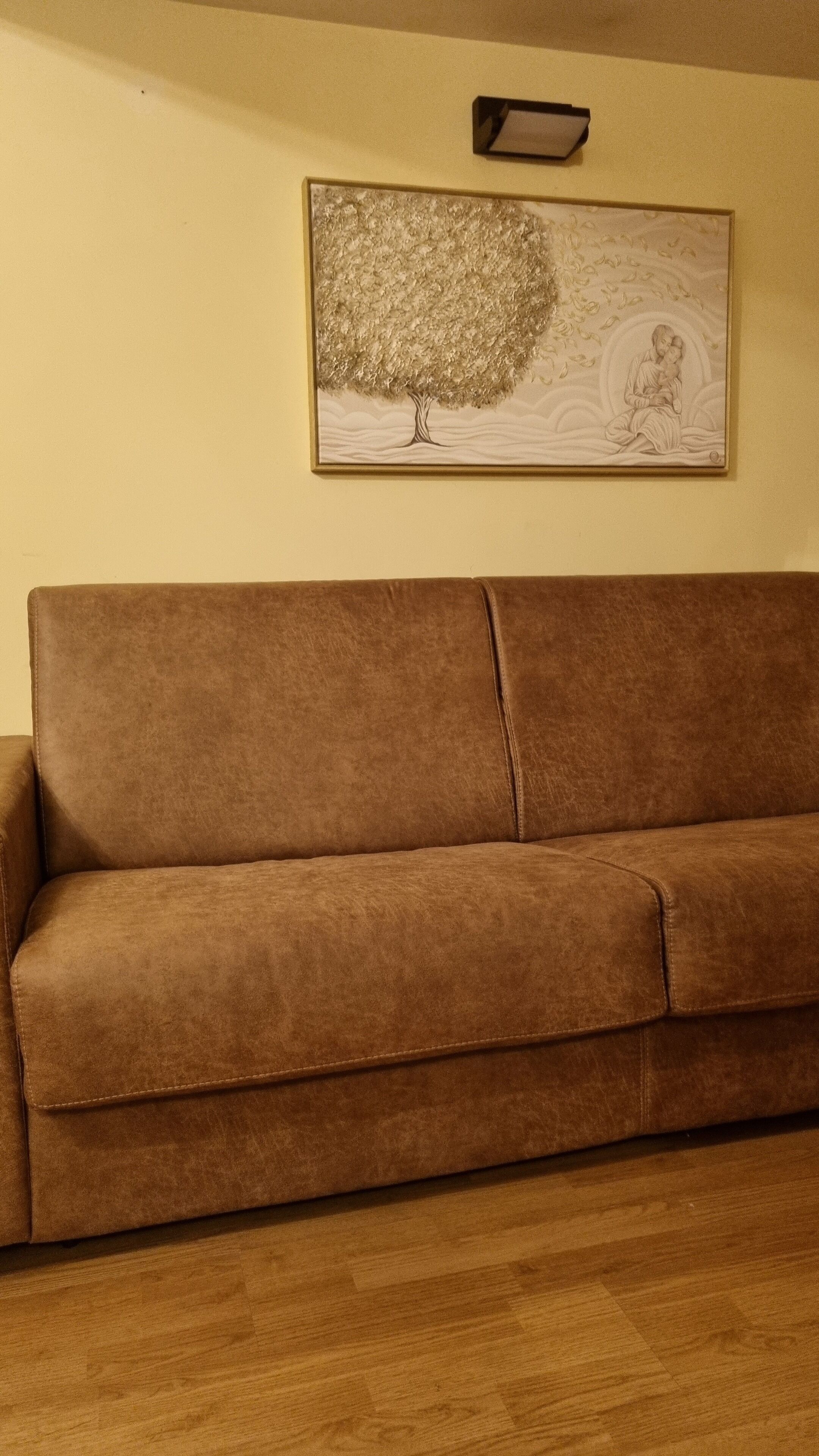 Ein braunes Sofa in einem Zimmer mit Holzboden und einem gerahmten Kunstwerk an der Wand.