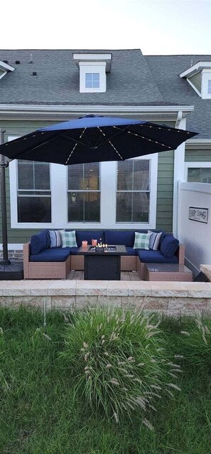 En terrasse med en blå parasol, en fletsofa med puder og et lille bord med stearinlys.