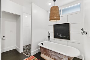 A bathroom with a vintage clawfoot bathtub, a woven light fixture, and a 'bonjour' sign on the wall.