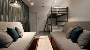 A compact room with two beds, a bunk bed, a wooden table, and a wall with a textured design.