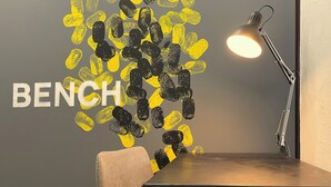 A room with a wall featuring a large 'BENCH' text and a pattern of yellow and black shapes. A desk lamp is on the desk.