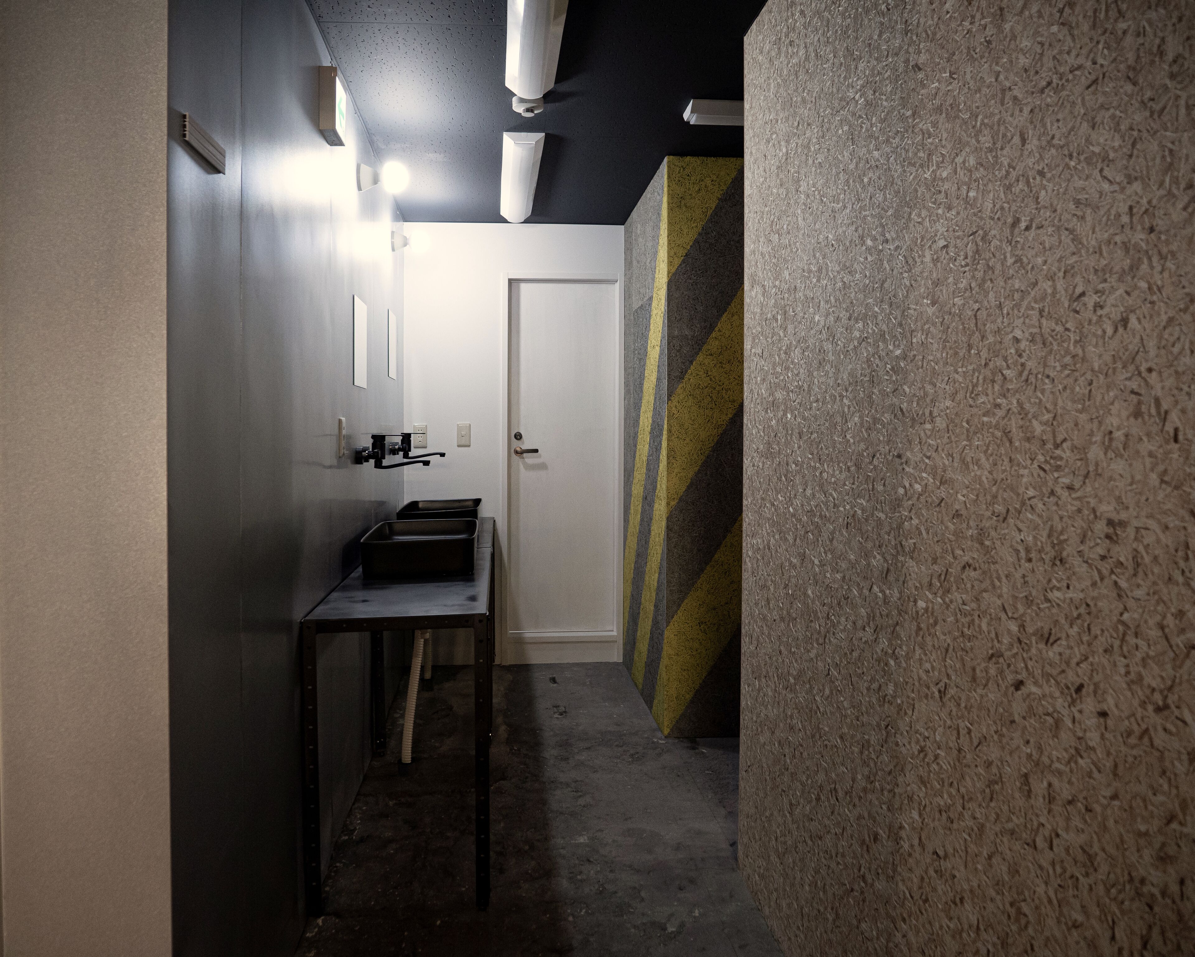 A narrow hallway with a sink and mirror on the left, a door at the end, and a textured wall on the right.