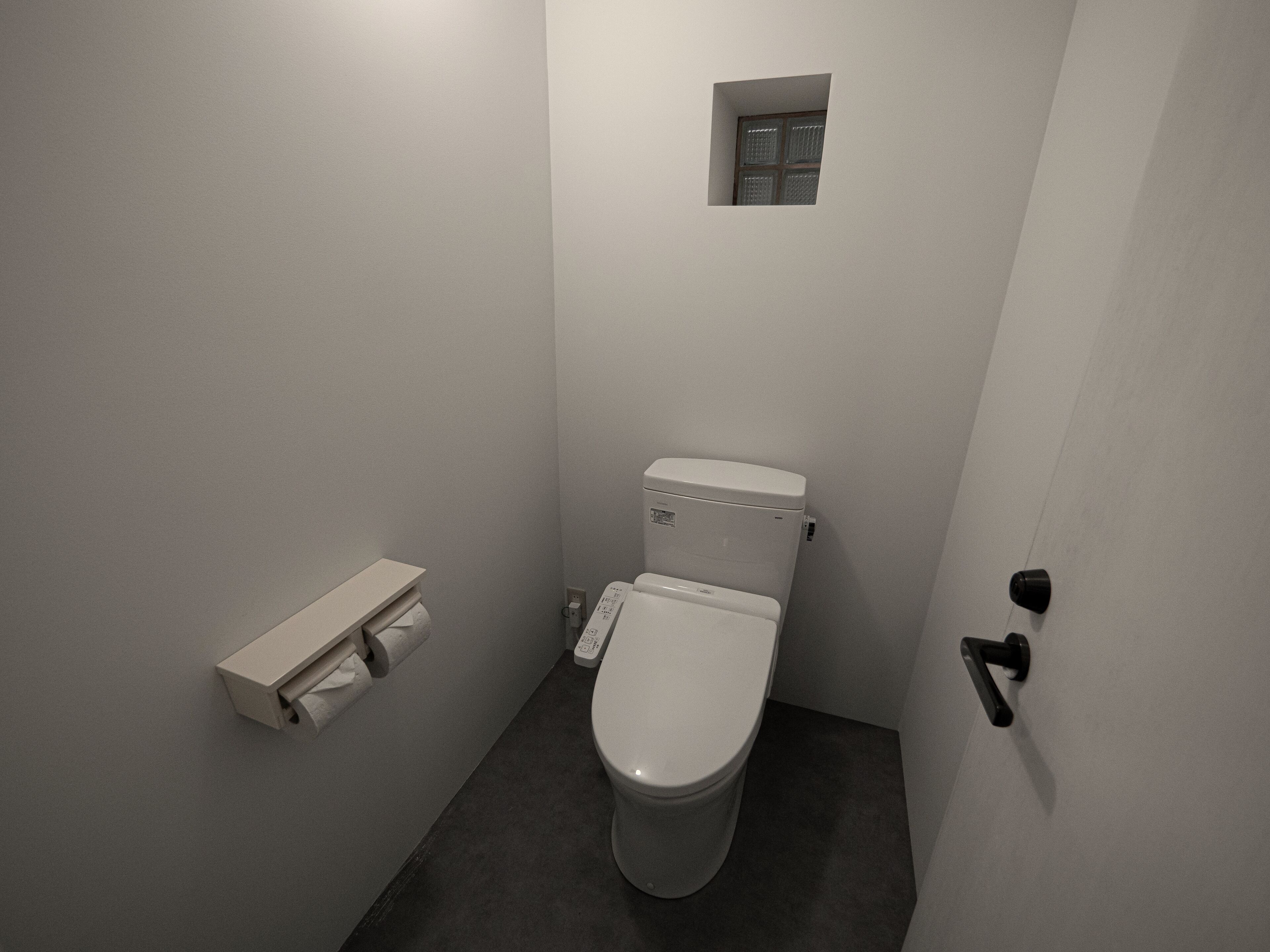 A small, narrow bathroom with a toilet, a small window, and a towel dispenser.