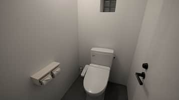 A small, narrow bathroom with a toilet, a small window, and a towel dispenser.