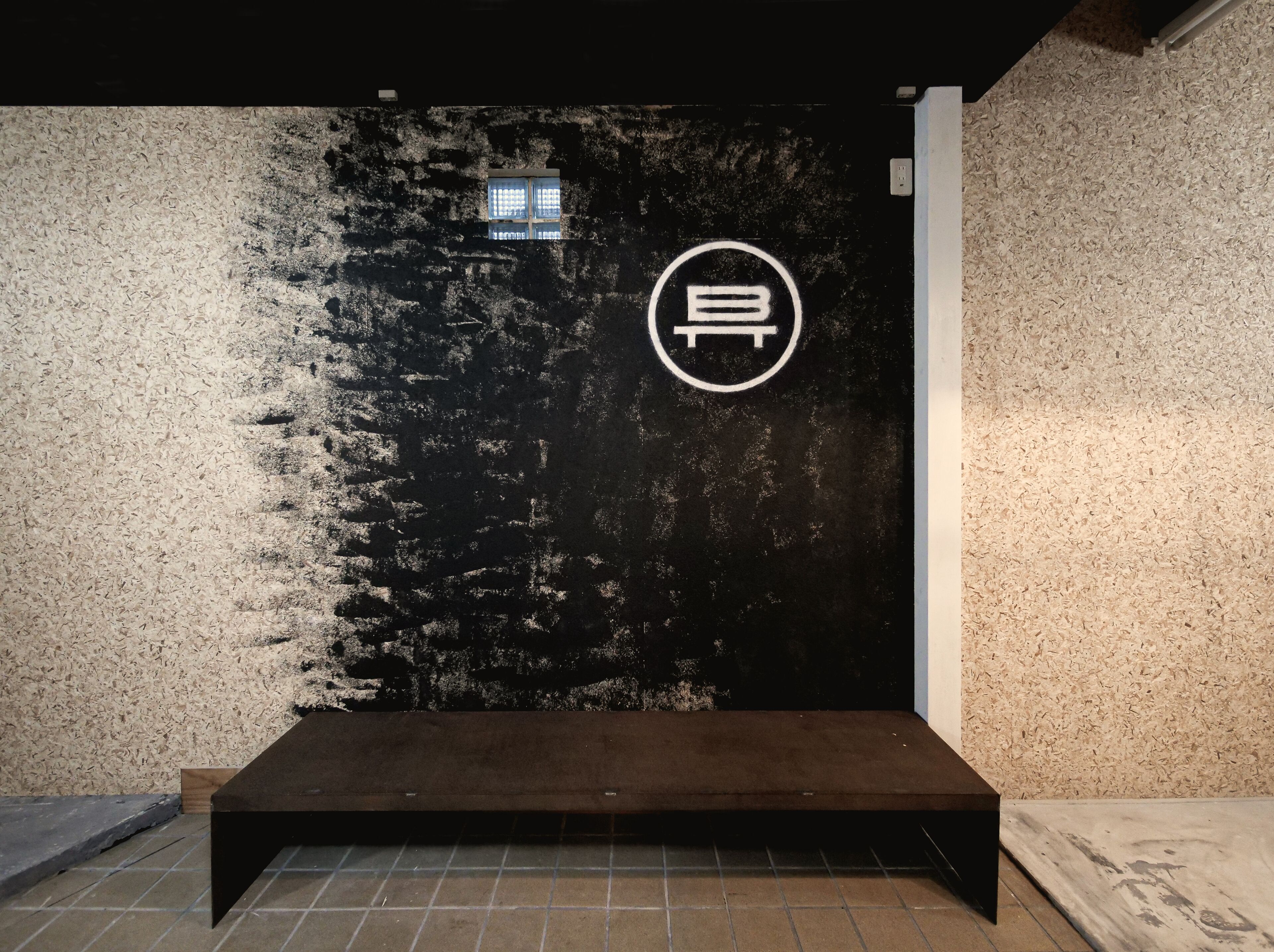 A dark wall with a textured surface and a circular logo.