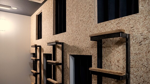 A hallway with wooden shelves and black frames against a textured wall.
