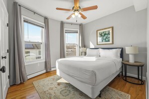 A bedroom with a bed, a ceiling fan, a window, a framed picture, and a nightstand with a lamp. - 4BR Near Downtown Boston Private Driveway Parking & 1-Min Walk to Train (Boston)