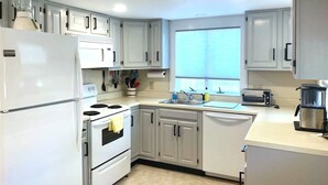 A modern kitchen with white cabinets, a built-in oven, a sink, and a window providing natural light. - Short 1/2 mile walk to the beach! Located in beautiful Harwich. (Harwich)