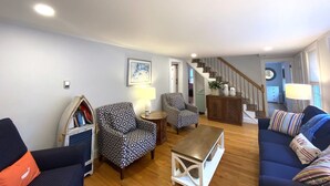 A living room with a sofa, two patterned armchairs, a coffee table, and a bookshelf. A staircase leads to another room. - Short 1/2 mile walk to the beach! Located in beautiful Harwich. (Harwich)