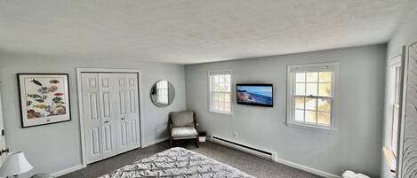 Ein Schlafzimmer mit einem großen Bett, einem Sessel, einem Fernseher und einer Tür.