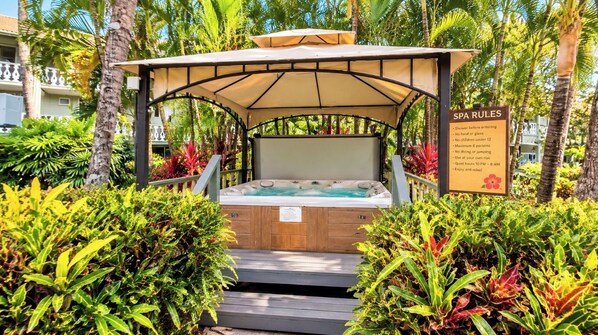 A spa area with a hot tub under a canopy, surrounded by lush greenery and a sign listing spa rules.