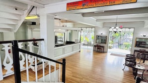 A spacious hotel lobby with a wooden floor, a staircase with a white railing, and a sign indicating the hotel name and rules.