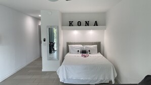 A modern bedroom with a bed, a mirror, and a wall-mounted sign reading "KONA".