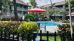 A hotel pool area with lounge chairs, umbrellas, and a fenced garden.