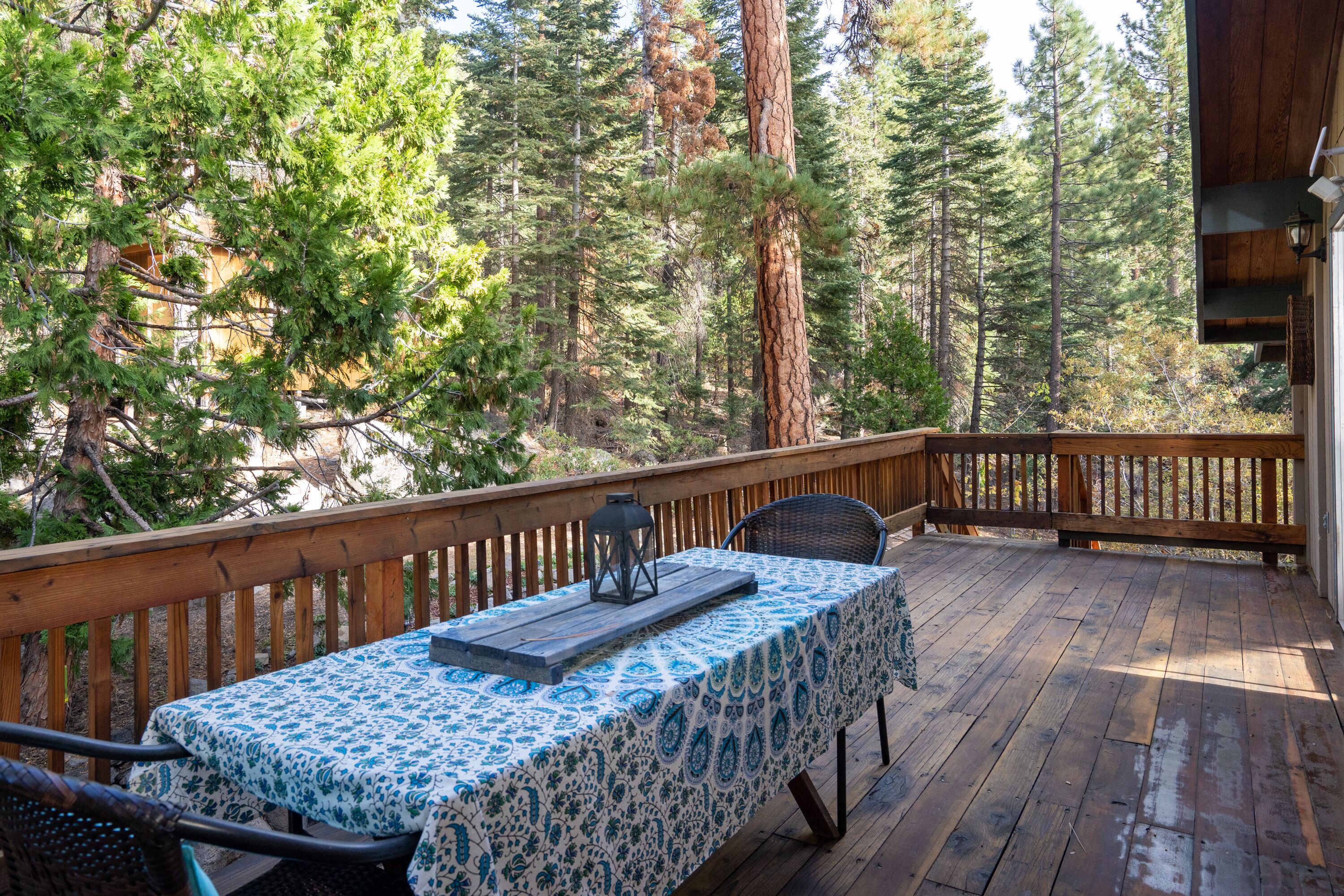 A wooden deck with a table set for two, surrounded by tall trees.