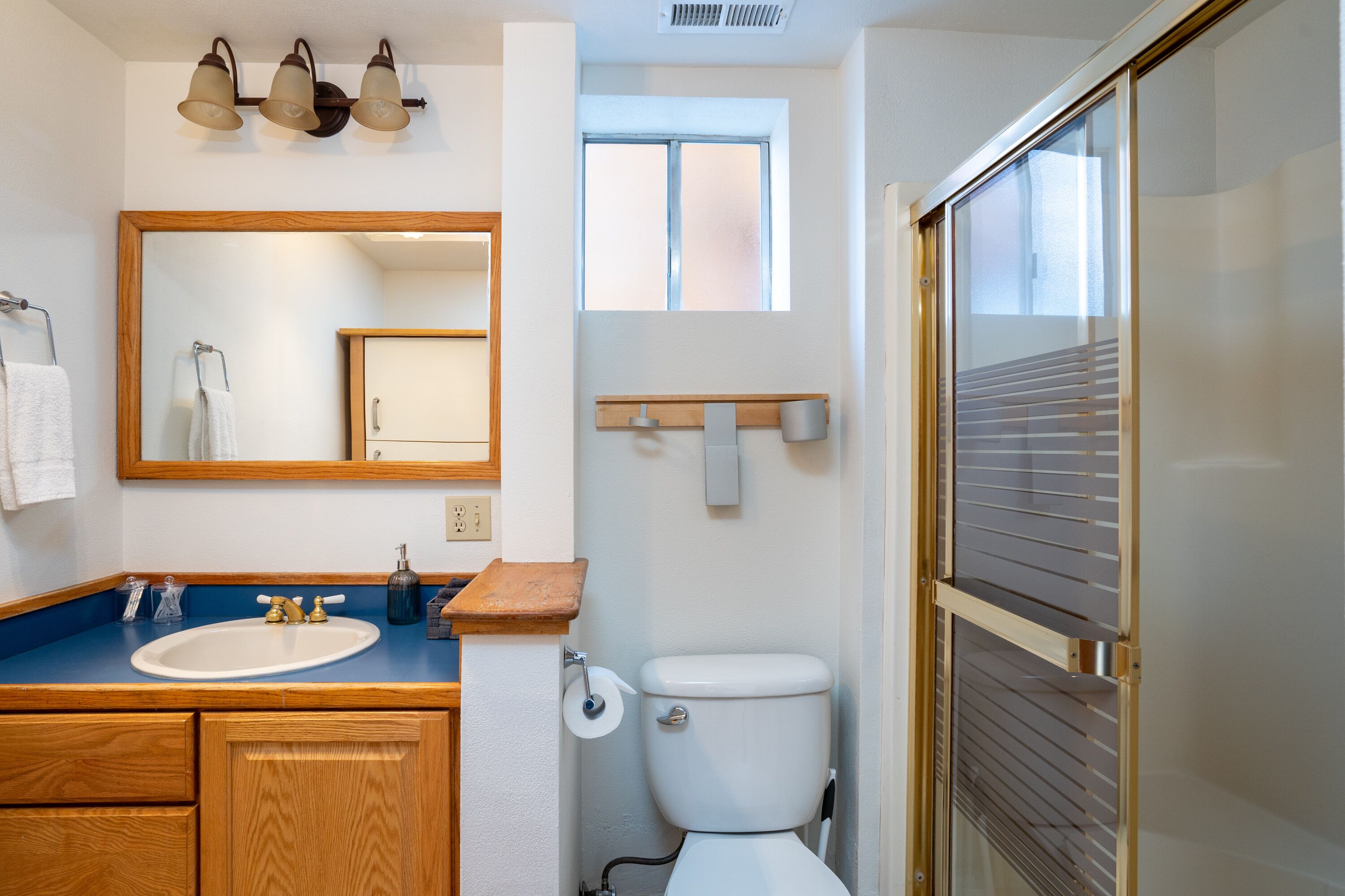 Un baño con tocador de madera, un espejo, un inodoro y una zona de ducha.
