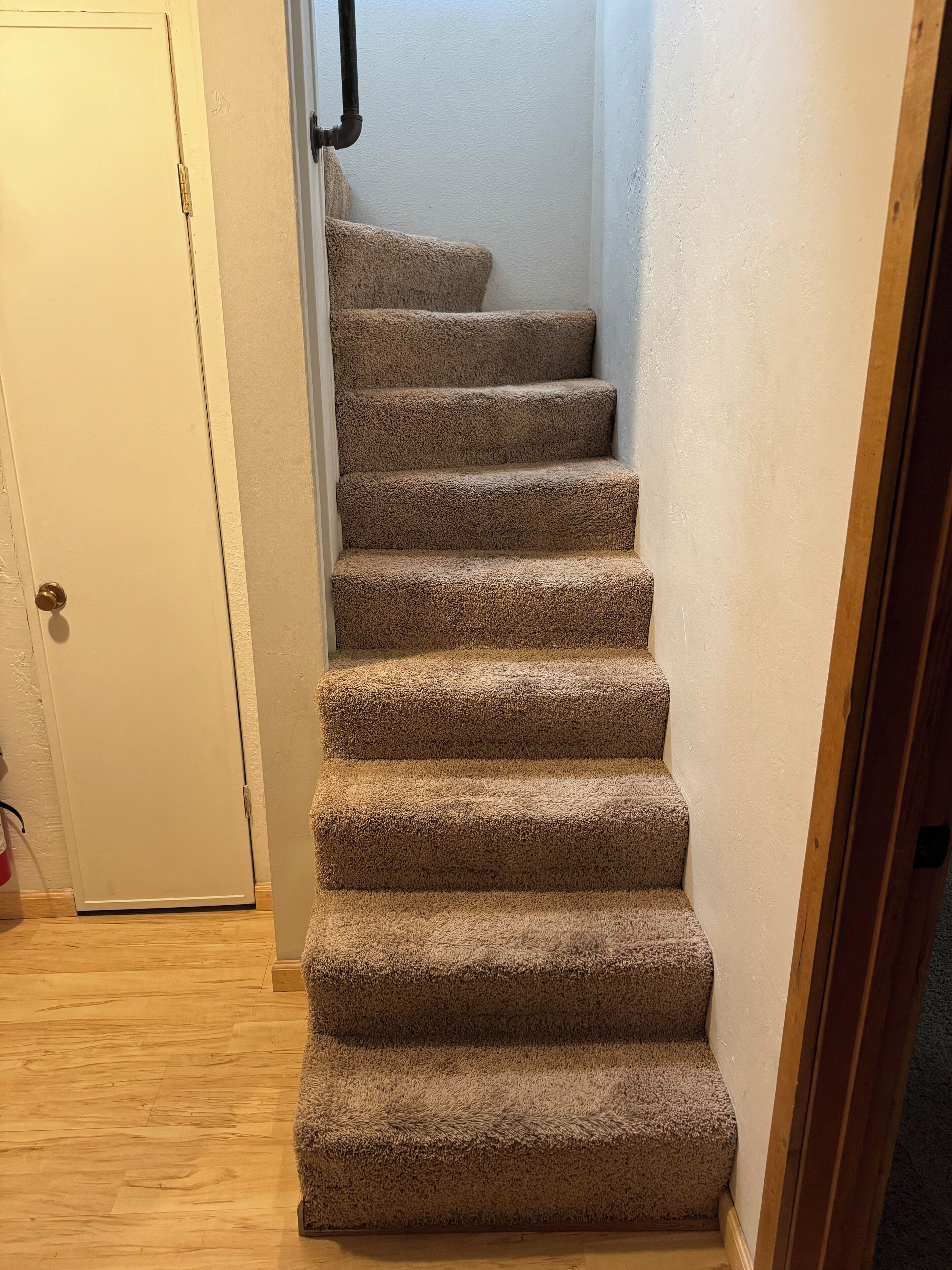 Una escalera empapelada con piso de madera y una puerta blanca al final.