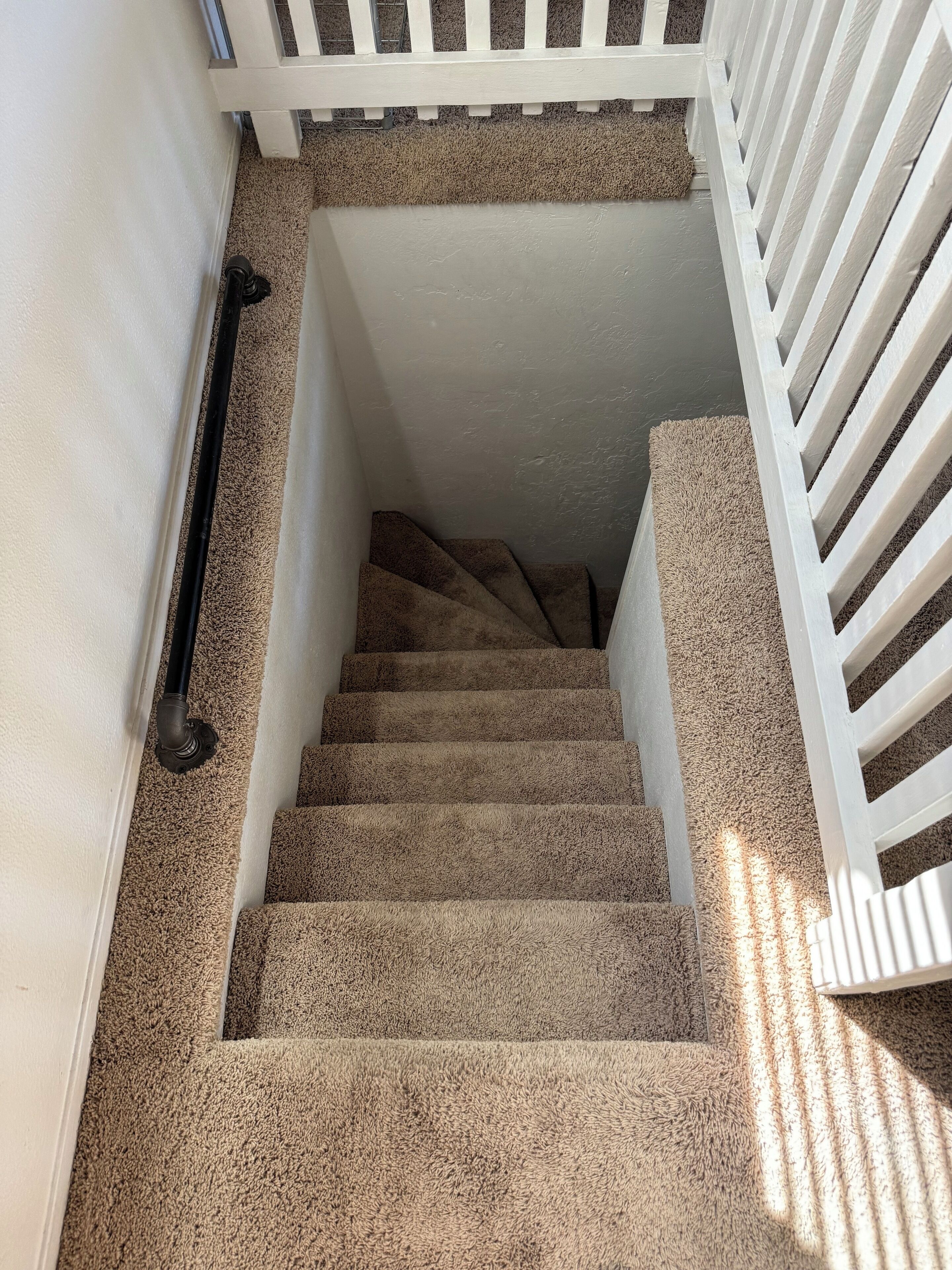 A carpeted staircase with a white railing and a handrail on the left side.