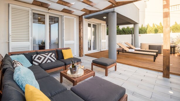 Un'area relax esterna moderna con un patio in legno, un divano e un tavolino con una bottiglia e dei bicchieri.