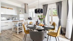 Una cucina moderna con mobili bianchi, una cappa in acciaio inossidabile e un'area pranzo con un tavolo rotondo per quattro persone.
