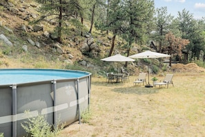 Piscina al aire libre con zona techada, rodeada de césped, sillas y sombrillas.
