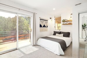 Un dormitorio moderno con una cama grande, un ventanal corredero a un balcón y vistas a árboles.