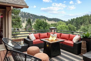 Terraza con mobiliario exterior, chimenea y vista a una ladera boscosa.
