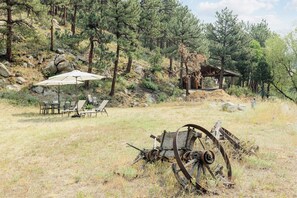 A rustic outdoor seating area with a table and chairs, surrounded by a natural landscape with trees and a wooden structure. - 6BR Mountain Retreat • Hot Tub • Walk to Pearl St (Boulder)