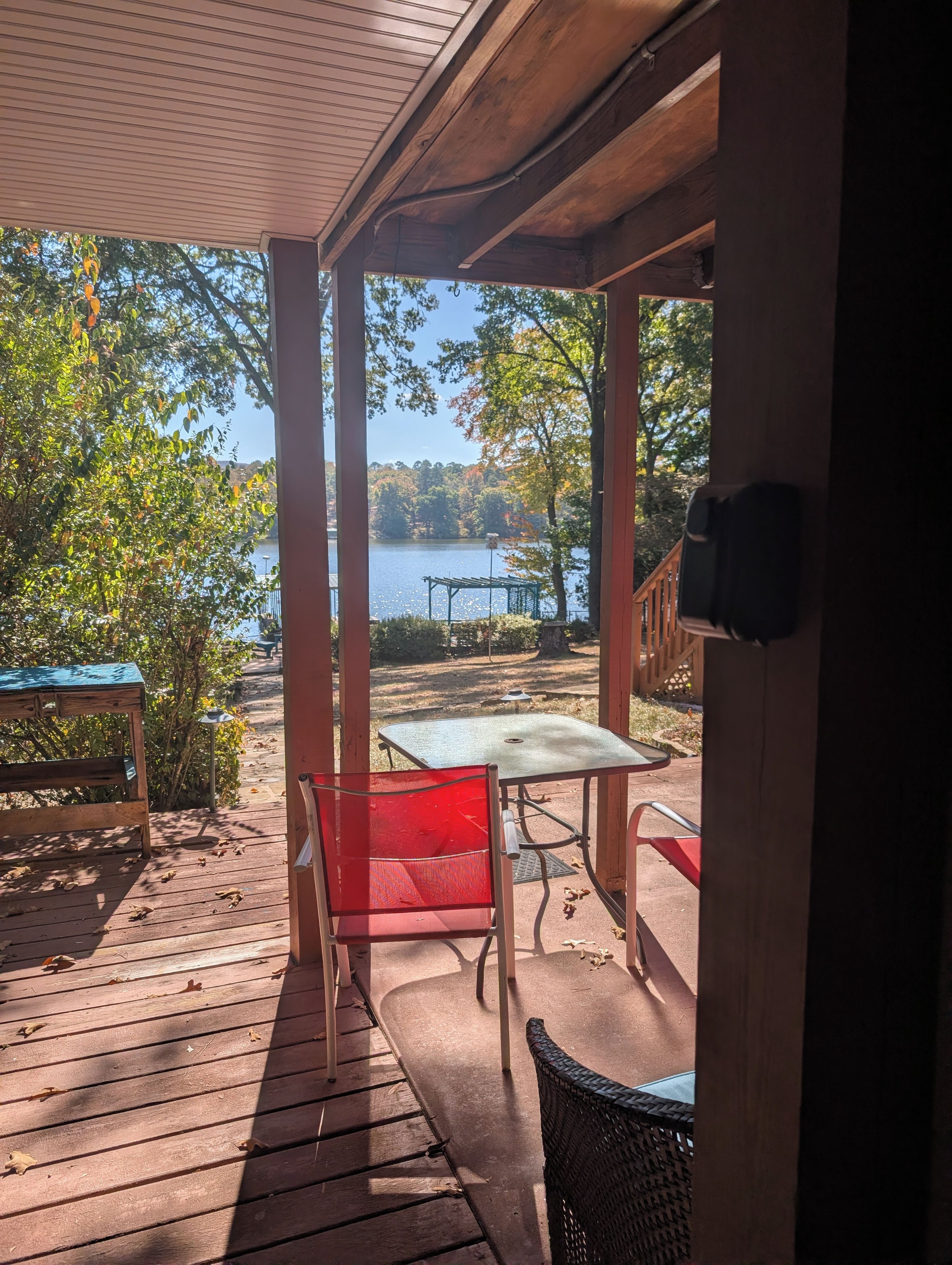 A wooden deck with a table and chairs, overlooking a lake with trees and a gazebo.