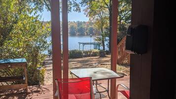A wooden deck with a table and chairs, overlooking a lake with trees and a gazebo.
