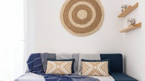 A neatly arranged bed with a striped bedspread, two pillows with geometric patterns, and a woven wall hanging above. - Tocco di Blu  SicilyMyHome (Santa Maria del Focallo)