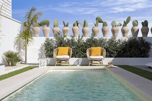Un área de piscina con dos sillas de mimbre, un muro de cactus y un edificio blanco.