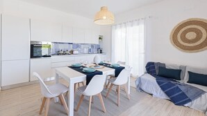 A modern kitchen with white cabinets, a dining table set with blue and white plates, and a hanging light fixture. - Tocco di Blu  SicilyMyHome (Santa Maria del Focallo)