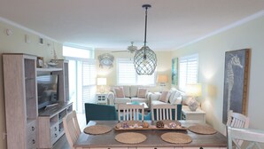 A living room with a TV, seating, and a dining area with placemats. - Gorgeous, oceanfront 2/2 villa in upscale Blue Water Keys North Myrtle Beach (North Myrtle Beach)