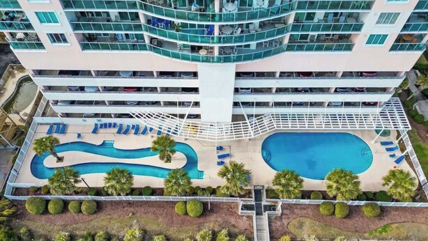 A multi-story hotel with a pool area, including a large pool and a smaller pool, surrounded by palm trees and lounge chairs. - Gorgeous, oceanfront 2/2 villa in upscale Blue Water Keys North Myrtle Beach (North Myrtle Beach)