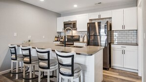 Une cuisine moderne avec des meubles blancs, des appareils en acier inoxydable et un îlot central doté de tabourets de bar.